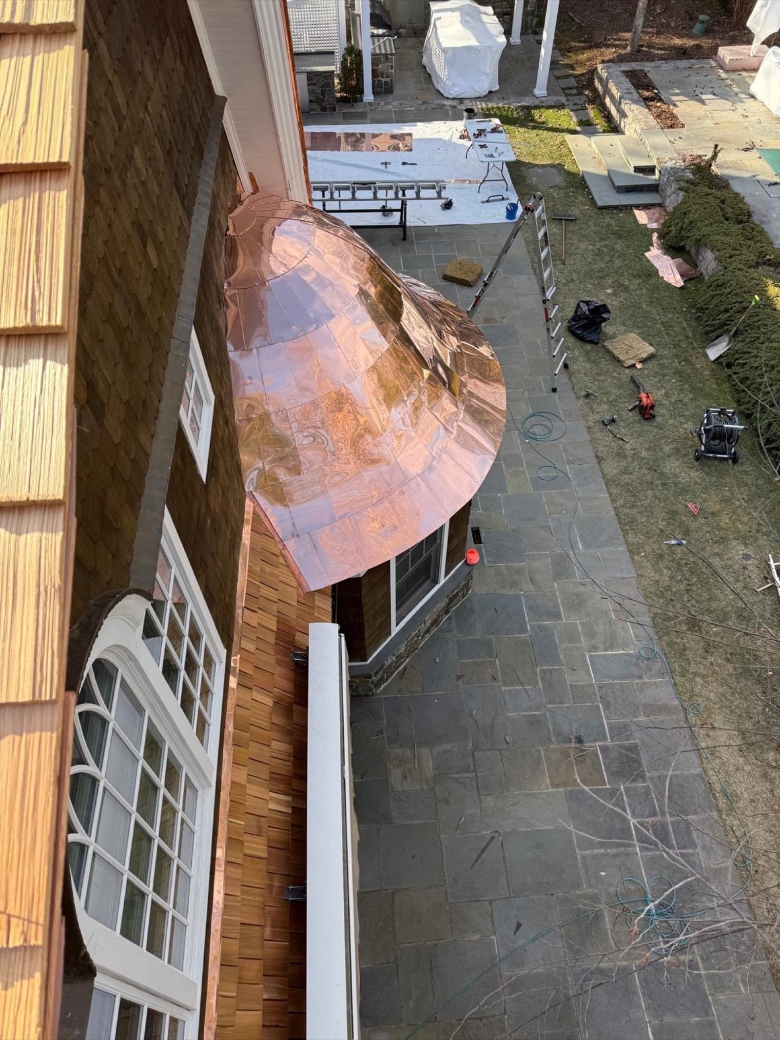 Curved copper bay-window roof on a cedar-shake luxury home — custom metal detail by Zubar Roofing.